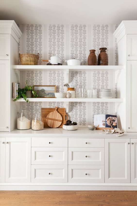 White and grey wallpaper behind the white shelves in a white kitchen