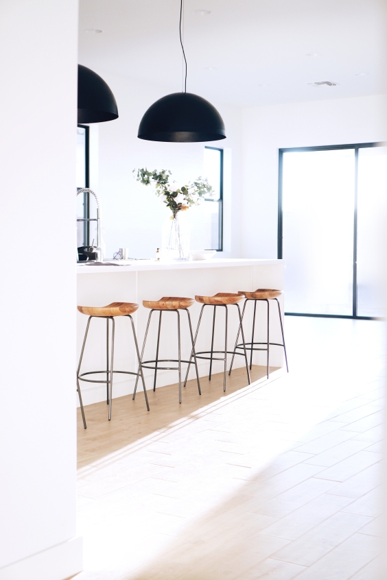 White kitchen island and wooden stoold with 2 oversized black ceiling lights