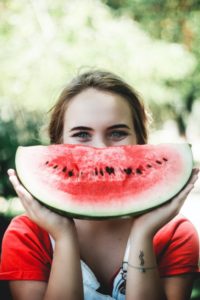 Girl holding a slice of watermelon under her ey